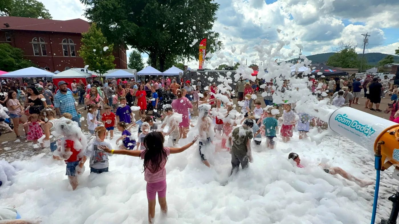 A large crowd enjoying an Elite Foam Experiences foam party at a community festival